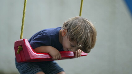 Child twisting and turning at playground swing playful little boy having fun by himself outside at...