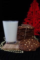 Chocolate cookies with pine nuts, glass of milk and Christmas tree and golden beads on the black ground. Dark and moody food photography. 