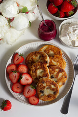 Cottage cheese pancakes with strawberries and a bowl of berries, jam, sour cream and peonies 