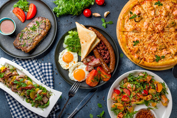 English Breakfast on a plate, pizza with seafood, salad with orange and salmon, steak striploin, salad with duck top view