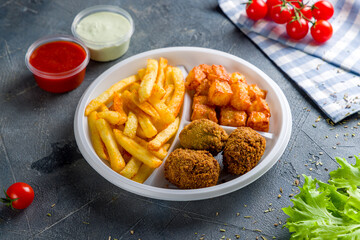 falafel balls in the dish with french fries and vegetables on grey concrete table