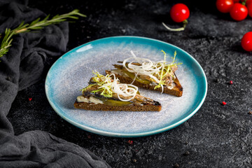 sprats on black bread on dark table