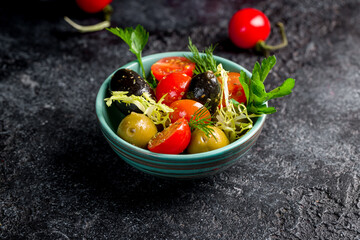 large olives with sliced tomatoes on bowl on dark table