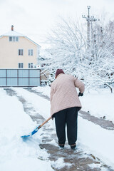 Winter problems concept . Woman digging snow with shovel at yard. Lady standing with blue shovel...