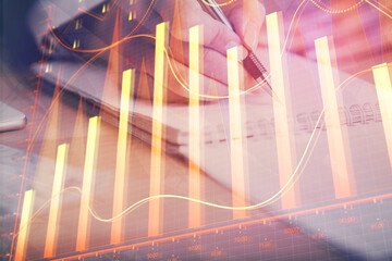 Naklejka premium A woman hands writing information about stock market in notepad. Forex chart holograms in front. Concept of research. Multi exposure