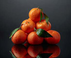 Tangerines or clementines with green leaves on a black background.