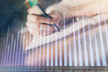 Financial forex graph displayed on hands taking notes background. Concept of research. Double exposure