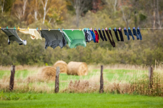 Clothing hanging to dry on a clothesline with a field and hay bales in the background, near Sault St. Marie; Ontario, Canada