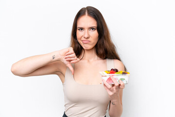 Young caucasian woman holding a bowl of fruit isolated on white background showing thumb down with negative expression