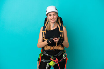 Young caucasian rock climber woman isolated on blue background sending a message with the mobile
