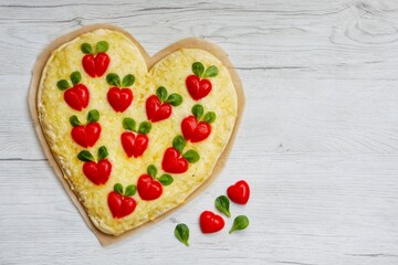 Heart shaped pizza with heart shaped tomatoes on parchment paper with white wood background.Creative art food idea for celebrate Valentine or Mother day.Top view.Copy space