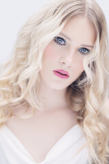 Young woman with blonde curly hair, blue eyes, pink lips and clear skin against a white background. Beauty photoshoot