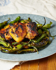 Grilled chicken with blistered shishito peppers on a metal plate.