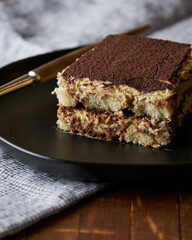 Classic tiramisu on a black plate with a dessert fork.