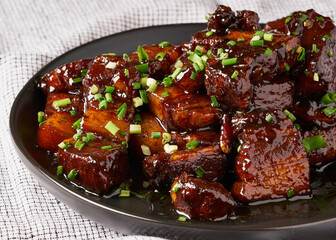A delectable pork belly dish is featured, glazed with a savory sauce and garnished with green...