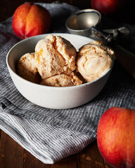 Peach ice cream in a white bowl with whole peaches