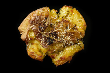 Smashed potato with parmesan cheese, salt and pepper on a solid black background