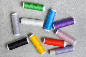 Reels with multi colored sewing threads gray concrete background.