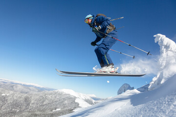Skier skiing and jumping downhill in high mountains against blue sky