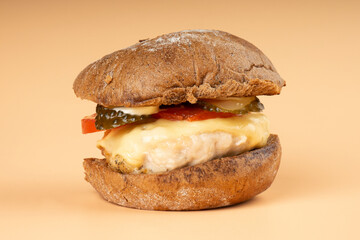 juicy burger with dark bun closeup, cheeseburger with chicken cutlet, cheese and vegetables on beige background