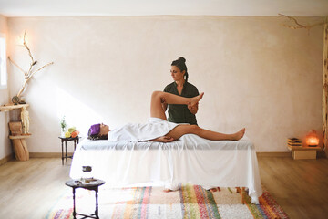 Massage room with general shot of masseuse bending patient's leg