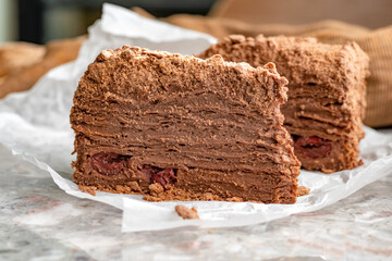 Napoleon cake with custard is decorated with cherries and grated chocolate on table.