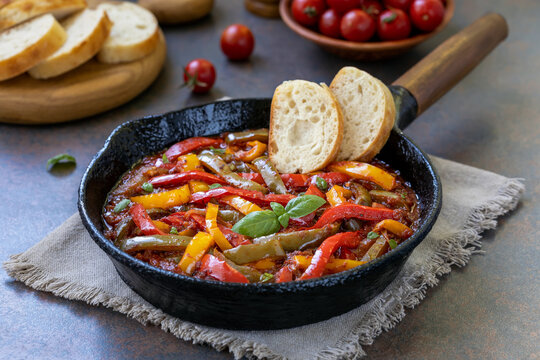 Italian sweet pepper stew Peperonata. Saut&eacute;ed red, yellow and green bell pepper in fresh tomato sauce with onion and olive oil served in frying pan with slices of white ciabatta bread.