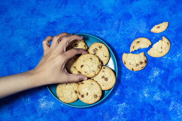 hand holding a homemade chocolate chip cookies on cutting board