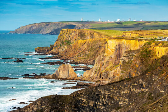 Dramatic rocky cliffed shoreline with the glow of sunset with large white satellite dishes in the background; Cornwall County, England