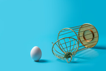 Upside down open cage with an egg outside on a blue background. The concept of liberation from...