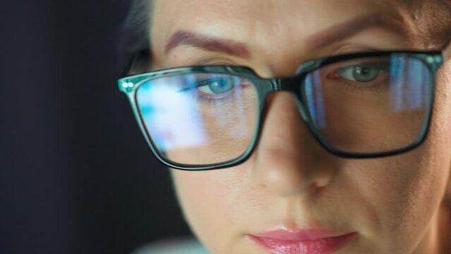 Woman in glasses looking on the monitor and working with charts at night