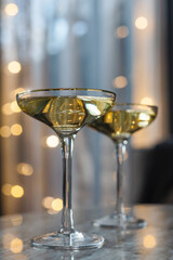 Two glasses of champagne against the background of a New Year's garland in a cozy living room.
