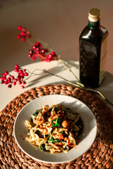 Farfalle pasta with mushrooms and spinach with bottle of olive oil on the white table