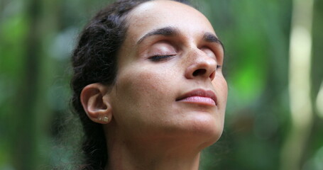 Woman meditating outdoors, taking a deep breath with eyes closed