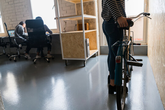 Faceless shot of woman standing with bicycle in office with people working on background.