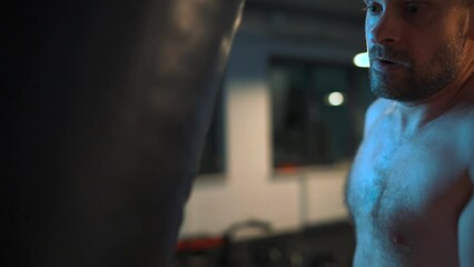 Alone boxer is working out blows on a punching bag in a gym in evening