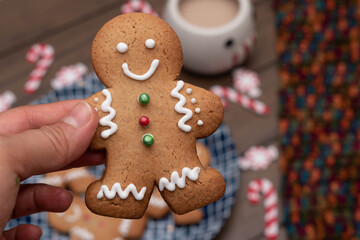 Woman hand holding a gingerbread man cookie with christmas decorations in the background