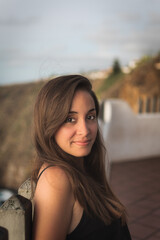 Portrait of a smiling woman with brown hair and black shirt, against a blue background at sunset.