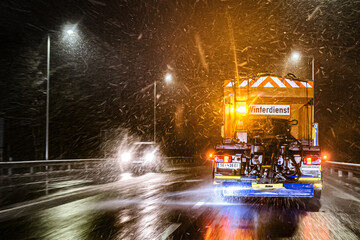 Ein Winterdienstfahrzeug verteilt Streusalz auf dem mit frisch gefallenem Schnee bedeckten Asphalt