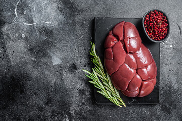 Beef veal kidney, raw offal meat on marble board with rosemary. Black background. Top view. Copy...