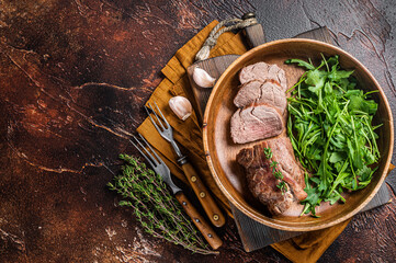 Juicy tenderloin Steak, sliced Roast beef in wooden plate with arugula. Dark background. Top view....