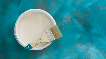 An open bucket with white paint on a blue background. There is a paint brush on the bucket. View...