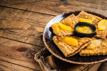 Traditional French crepe Suzette with orange sauce on a plate. Wooden background. Top view. Copy space