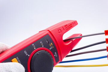 The electrician measures the current in the phase wire with a meter on a gray background
