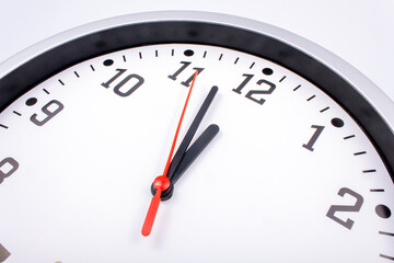 Midnight is coming. Black and white office clock with a red pointer on a gray background.
