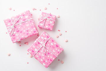 Fototapeta na wymiar Saint Valentine's Day concept. Top view photo of pink gift boxes in wrapping paper with heart pattern and sprinkles on isolated white background