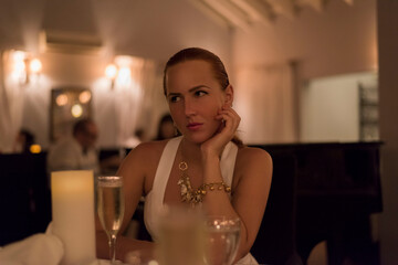 Young woman sitting in elegant dress in restaurant and having glass of champagne 