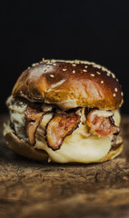 
Tasty beef, cheese, burger with many slices of bacon, warm coming out of smoke on a wooden cutting board on a black background, 
