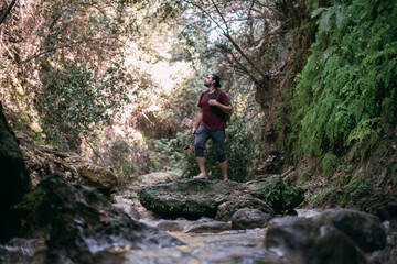 A young male tourist walks along a shallow tropical mountain river among the rocks.