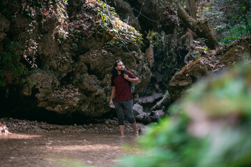 Obraz premium A young male tourist walks along a shallow tropical mountain river among the rocks.